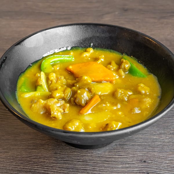 Close-up of a black bowl filled with yellow curry, green peppers, and carrots.