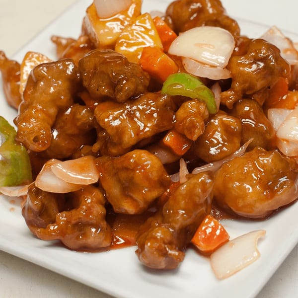 Sweet and sour chicken with pineapple, onions, and bell peppers on a white plate from Go China Restaurant.