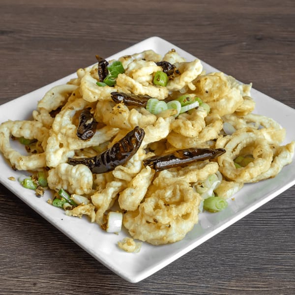Crispy fried calamari with green onions and dried red chilies on a white plate.