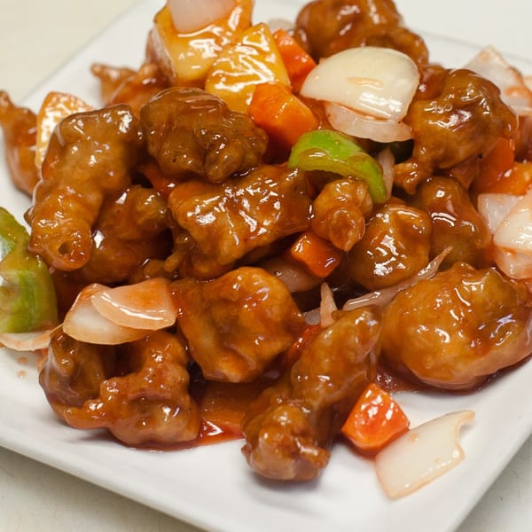 Sweet and sour chicken with pineapple, onions, and bell peppers on a white plate.